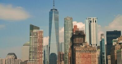 The Lower Manhattan skyline on a clear day, with the spire of One World Trade Center rising above surrounding glass and brick towers