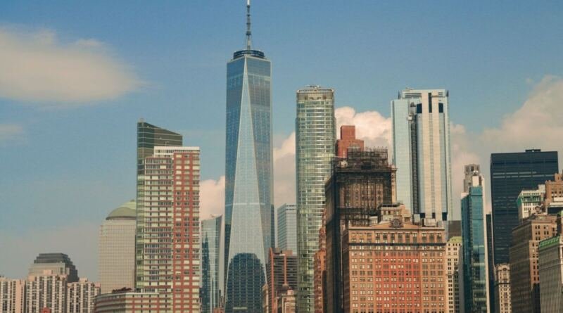 The Lower Manhattan skyline on a clear day, with the spire of One World Trade Center rising above surrounding glass and brick towers
