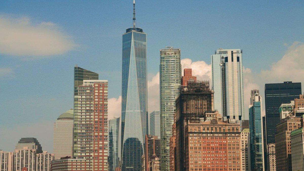 The Lower Manhattan skyline on a clear day, with the spire of One World Trade Center rising above surrounding glass and brick towers
