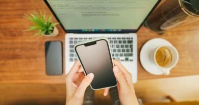 Hands holding a smartphone above an open laptop, illustrating AI email tools tested against a real 144-thread inbox.