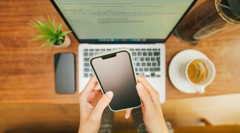 Hands holding a smartphone above an open laptop, illustrating AI email tools tested against a real 144-thread inbox.