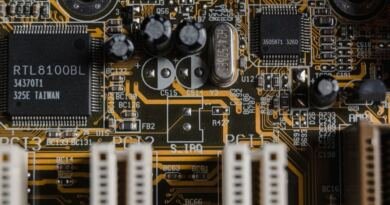 Close-up of a green computer motherboard, with a black RTL8100BL chip, silver capacitors and cream PCI slots on orange copper traces, illustrating the Apple M5 Ultra chip