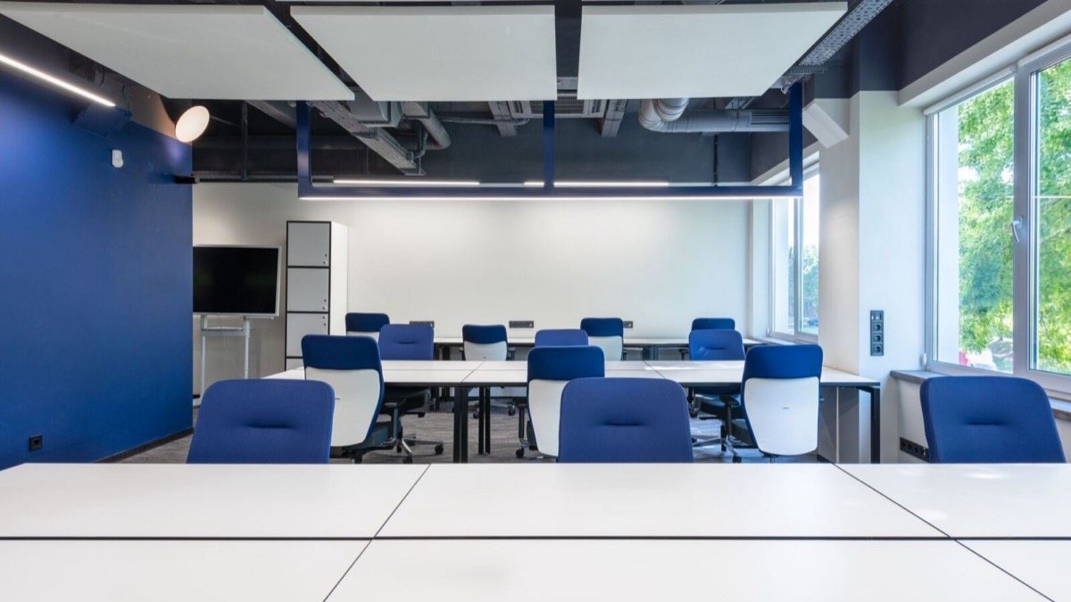 Empty blue chairs and white desks in a bright, unoccupied meeting room, the unfilled seats at the centre of the future of AI at work