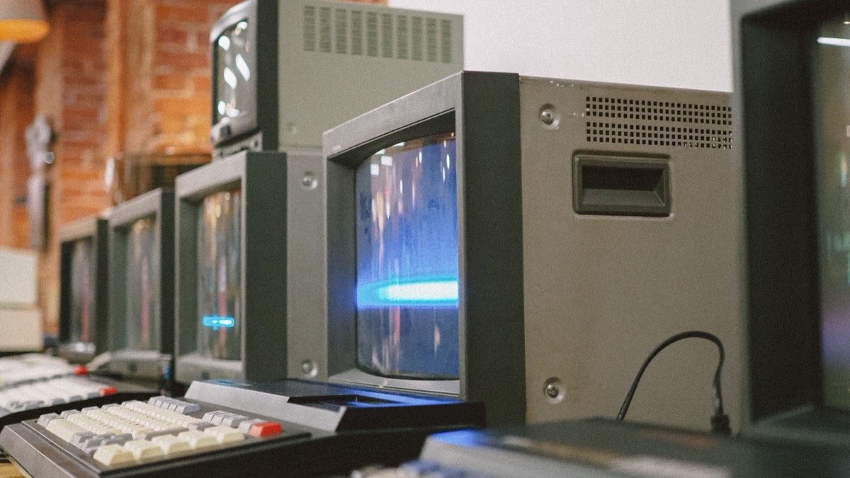 A row of vintage CRT computer terminals, illustrating the history of AI from the 1955 Dartmouth proposal to today.