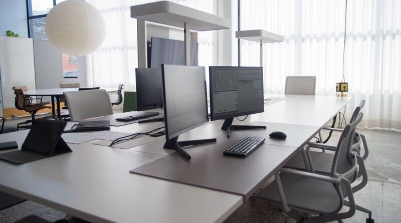 Empty desks with monitors in an open-plan office, illustrating AI tools for business priced per seat.