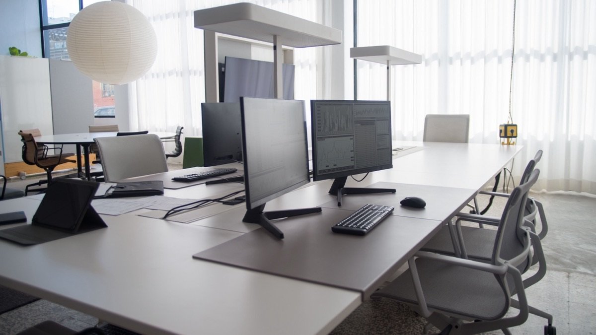 Empty desks with monitors in an open-plan office, illustrating AI tools for business priced per seat.