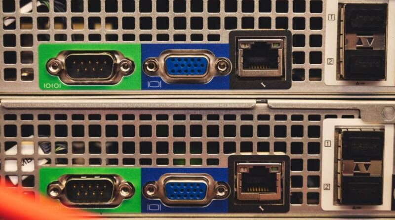 Close-up of the rear panels of two rack-mounted servers, showing green serial ports, blue VGA ports, Ethernet sockets and vented metal casing, illustrating Ox Alpha