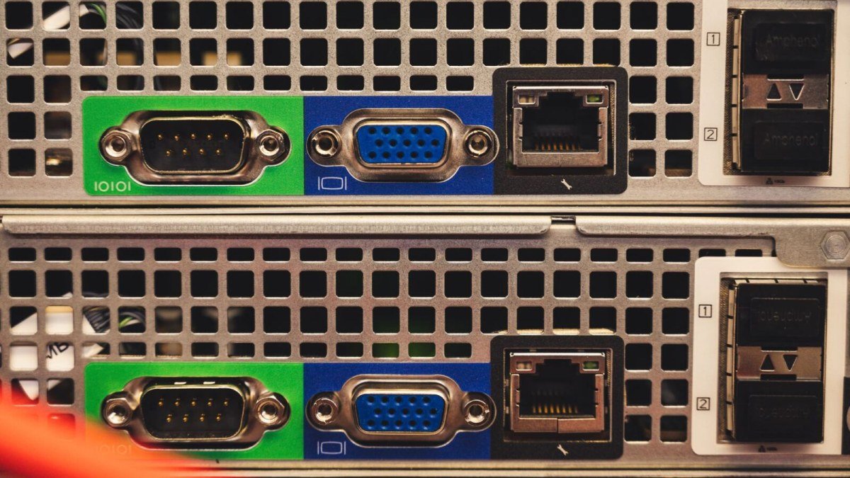 Close-up of the rear panels of two rack-mounted servers, showing green serial ports, blue VGA ports, Ethernet sockets and vented metal casing.