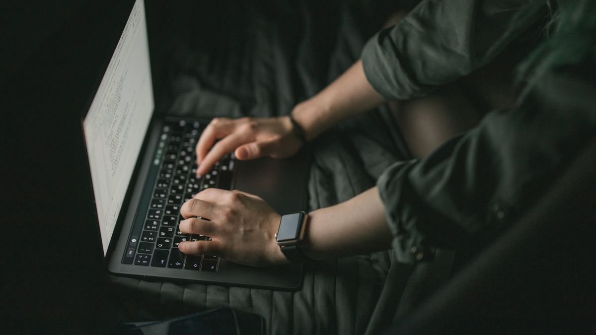 Hands typing on a laptop in low light, the human feedback stage in how RLHF works