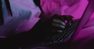 A person typing on a laptop under pink light, drafting with AI prompting techniques