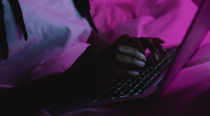 A person typing on a laptop under pink light, drafting with AI prompting techniques