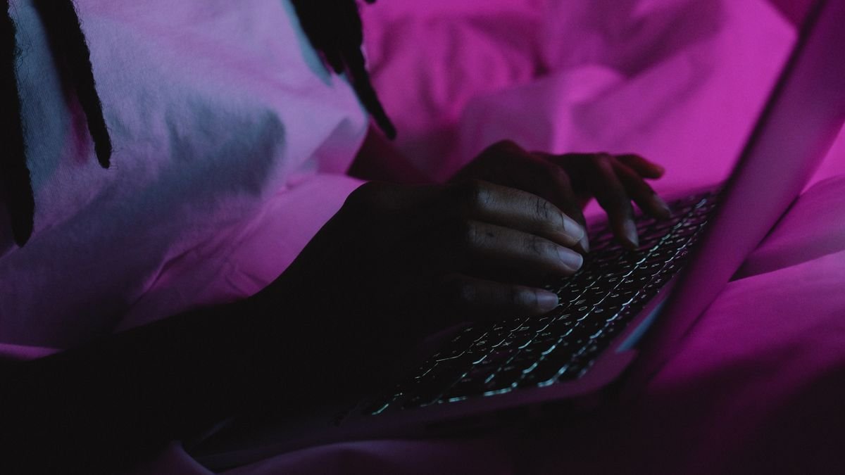 A person typing on a laptop under pink light, drafting with AI prompting techniques
