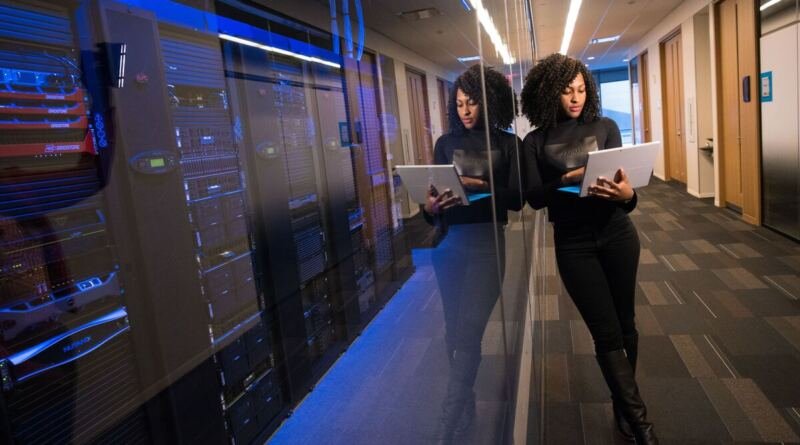 An engineer holds a laptop beside a lit server room, weighing an artificial intelligence platform seat against running the GPU itself.