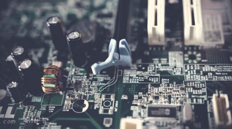 Macro photo of a green computer motherboard with capacitors, a copper coil and white expansion slots