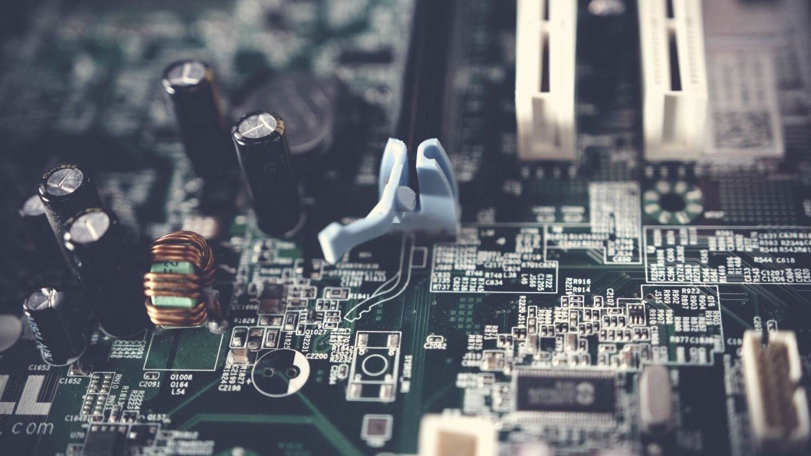 Macro photo of a green computer motherboard with capacitors, a copper coil and white expansion slots