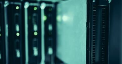 A blade server pulled part way out of a dark equipment rack, with green status lights glowing on the units behind it, illustrating the M6 Mac mini