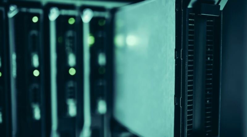 A blade server pulled part way out of a dark equipment rack, with green status lights glowing on the units behind it, illustrating the M6 Mac mini
