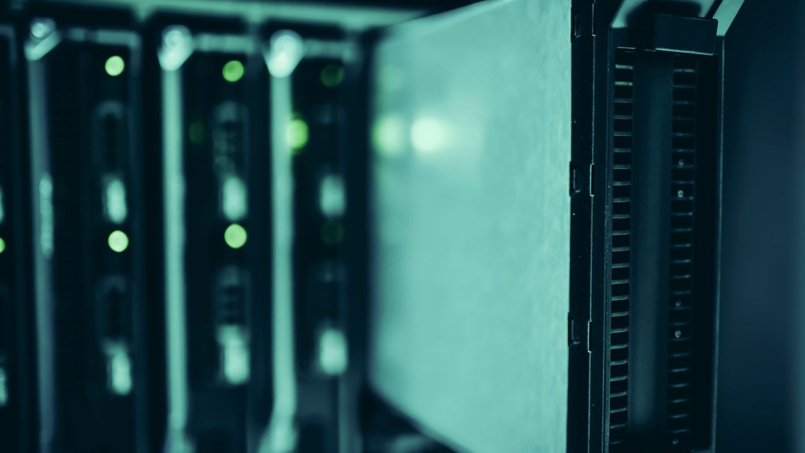 A blade server pulled part way out of a dark equipment rack, with green status lights glowing on the units behind it