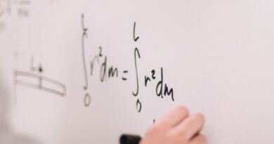 Close-up of a hand holding a black marker, writing integral equations in green and black ink on a white whiteboard.