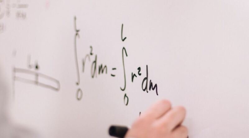 Close-up of a hand holding a black marker, writing integral equations in green and black ink on a white whiteboard.