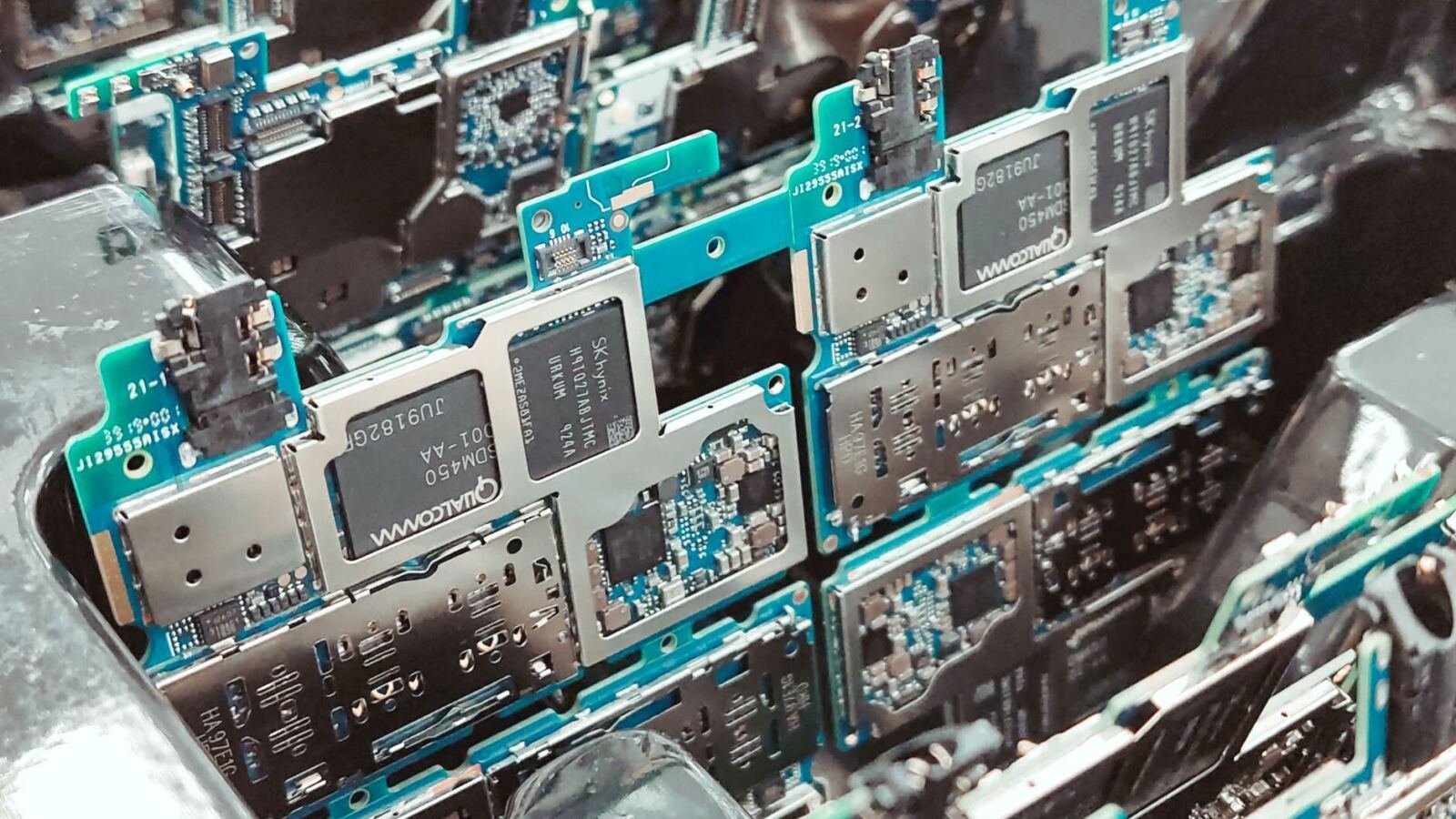 Close-up of stacked green smartphone circuit boards with silver metal shielding cans and Qualcomm and SK hynix chips