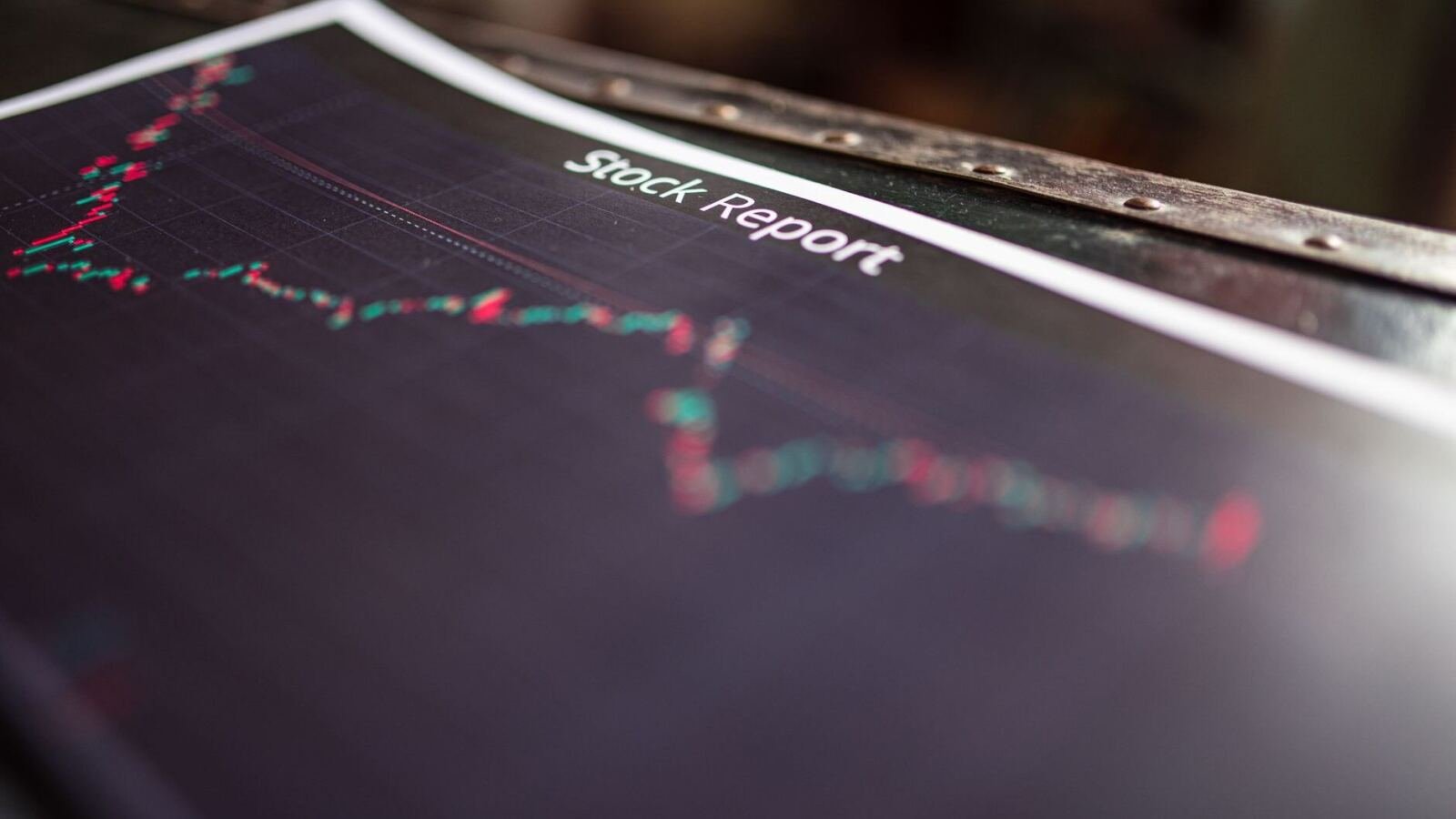 A printed stock report page with a red and green candlestick chart, lying on a dark wooden table