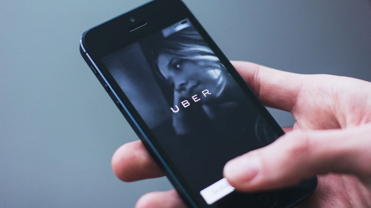A hand holding a smartphone displaying the Uber app launch screen