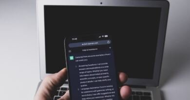 A hand holds a smartphone running one of the AI apps, a chatbot reply filling the screen, with an open laptop out of focus behind it