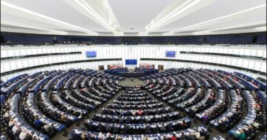 Rows of curved wooden desks and blue seats in the European Parliament hemicycle in Strasbourg during a plenary session, seat of the legislature that has AI defined in binding law.