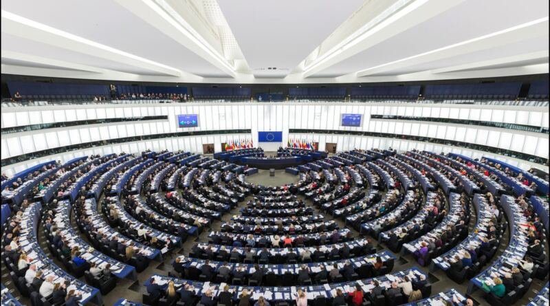 Rows of curved wooden desks and blue seats in the European Parliament hemicycle in Strasbourg during a plenary session, seat of the legislature that has AI defined in binding law.