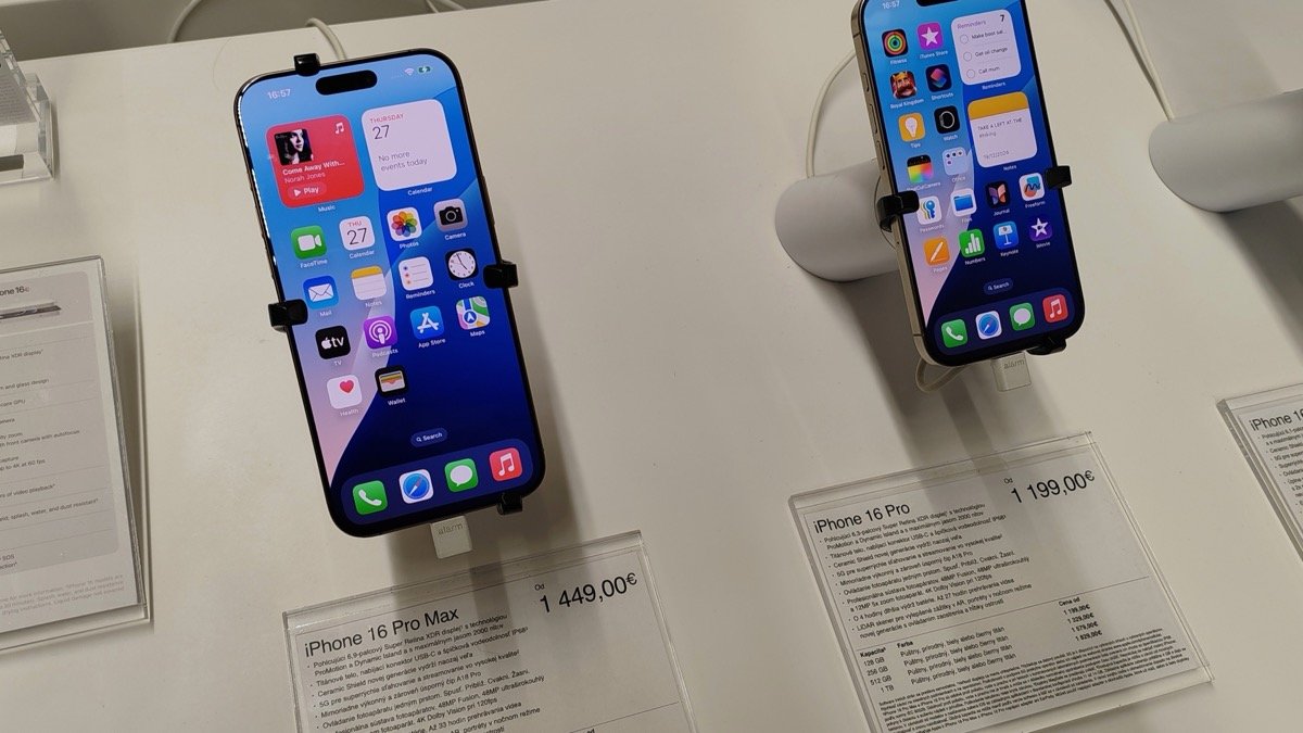 Two iPhone 16 Pro handsets clamped to stands on a white retail display table, each above a printed price card