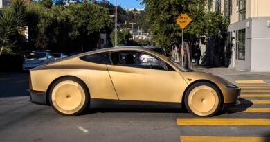 A gold two-door Tesla Cybercab, subject of the Tesla Cybercab NHTSA audit, stopped at a crosswalk on a tree-lined San Francisco street