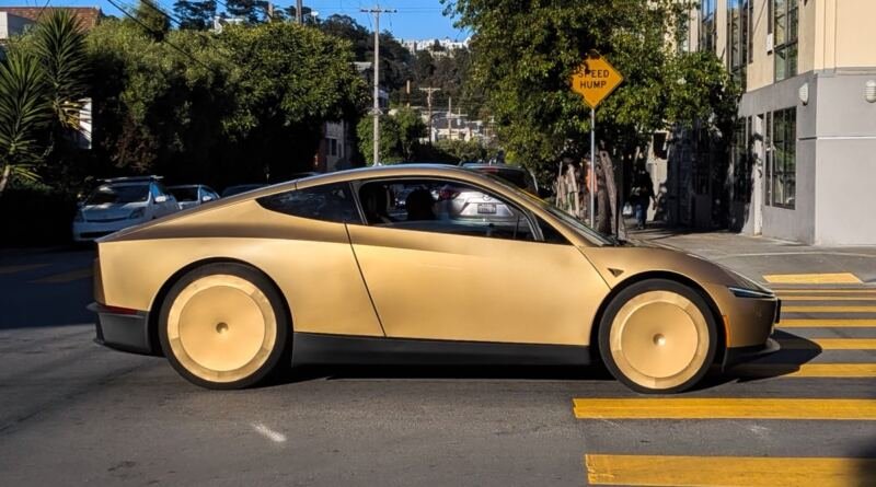 A gold two-door Tesla Cybercab, subject of the Tesla Cybercab NHTSA audit, stopped at a crosswalk on a tree-lined San Francisco street