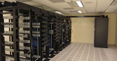 A row of tall black server racks with cable management arms and blue patch cables in a data centre, illustrating the hardware layer of the ai technology stack