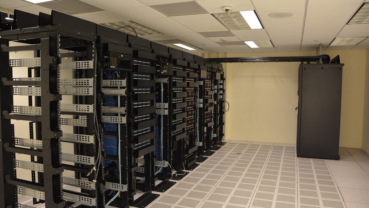 A row of tall black server racks with cable management arms and blue patch cables in a data centre, illustrating the hardware layer of the ai technology stack