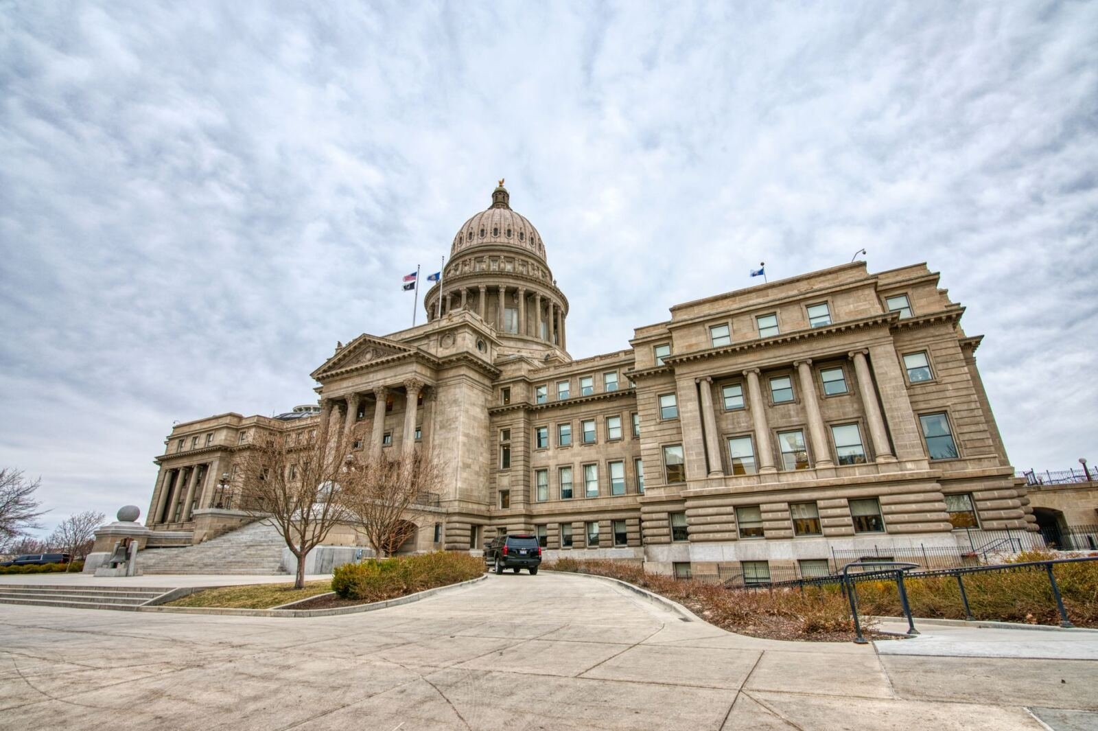 A sandstone capitol building with a domed rotunda and a columned portico, photographed from the driveway under a cloudy sky