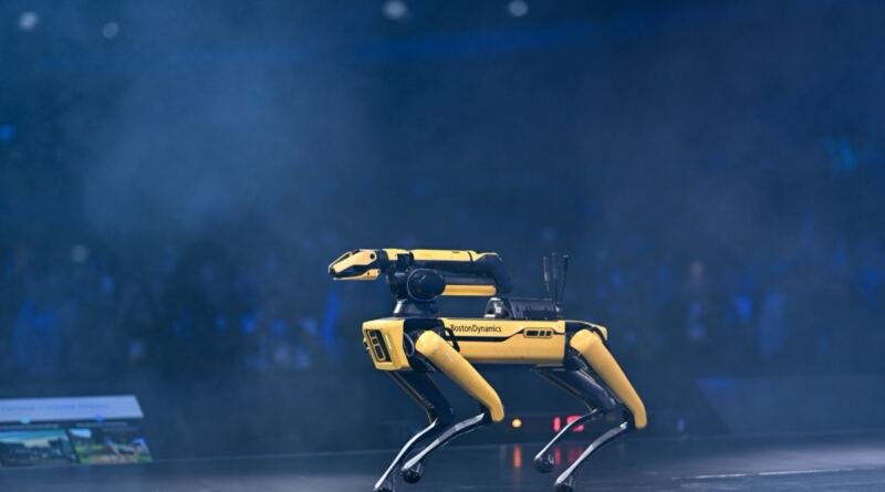 Yellow Boston Dynamics Spot quadruped robot on a dark stage, illustrating the FieldAI $700M term sheet
