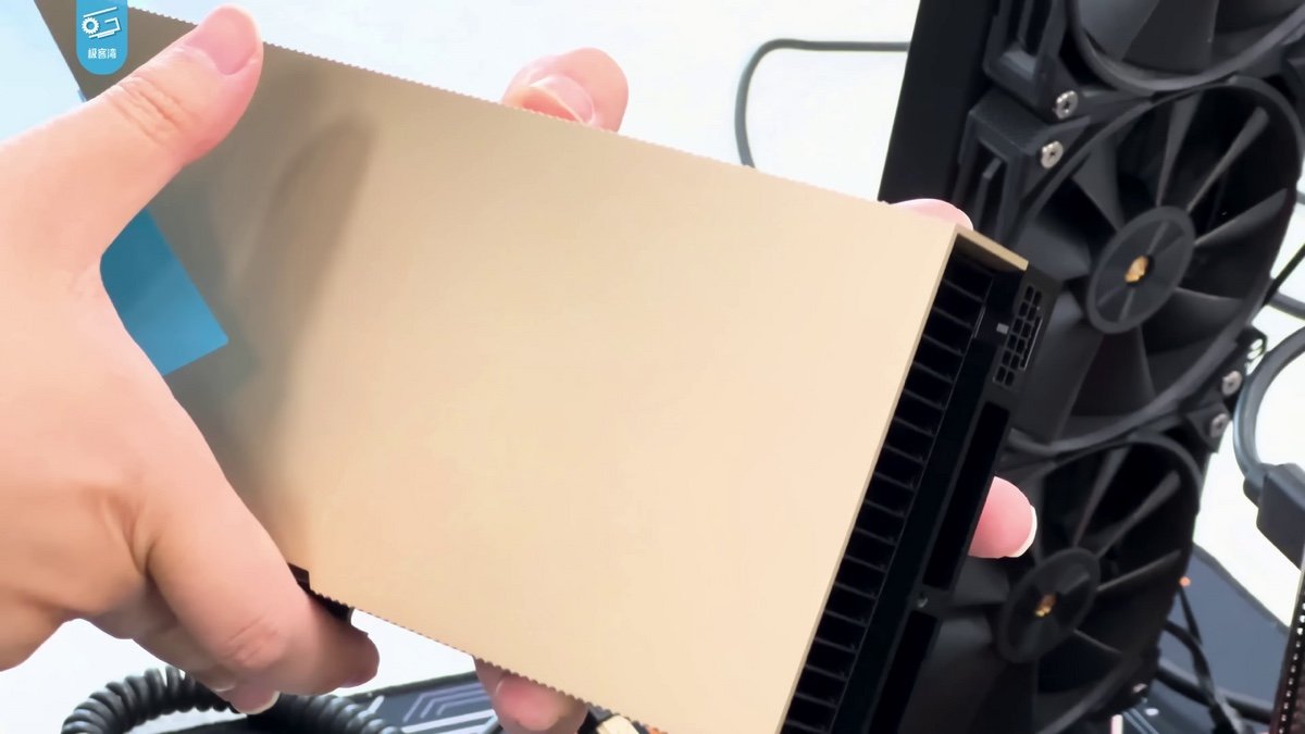 Hand holding a gold Nvidia H100 accelerator card beside an open PC, illustrating the Nvidia chip smuggling indictment