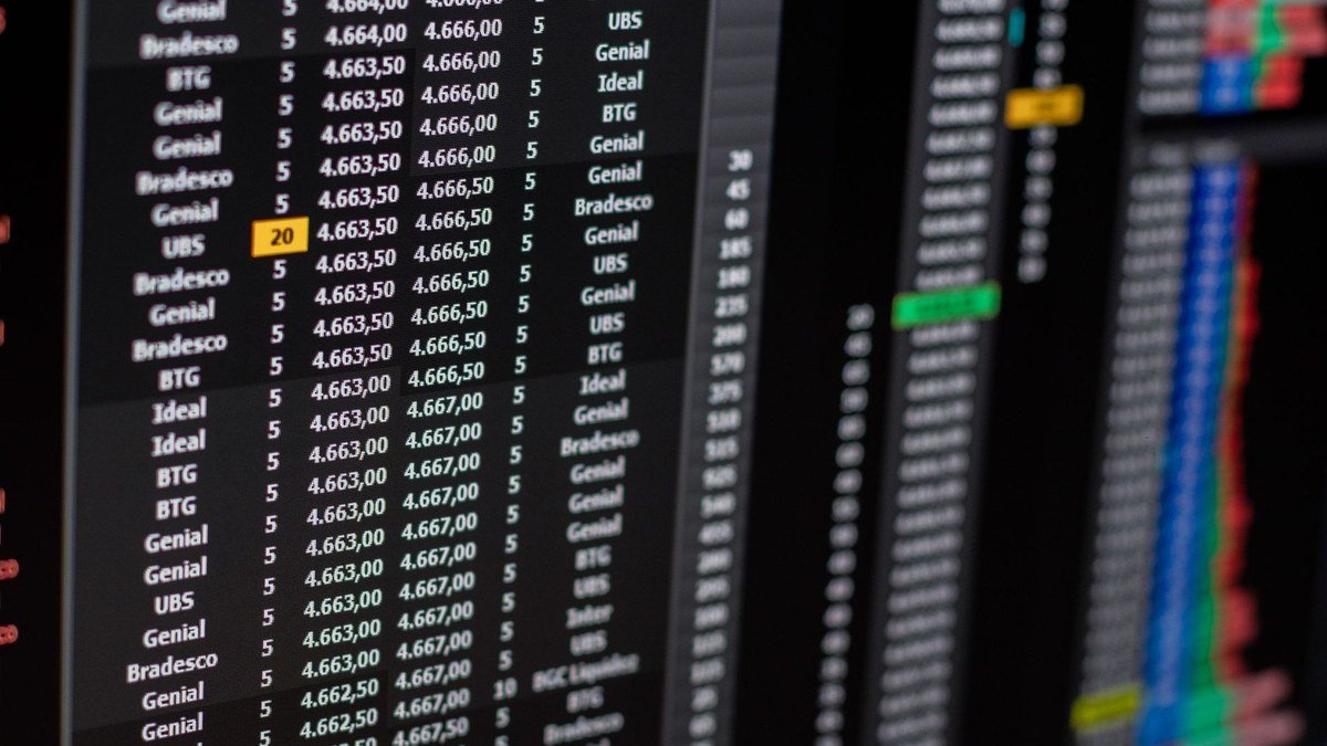 Close-up of a dark trading terminal screen showing an order book of broker names beside bid and ask prices, with blurred price charts to the right.