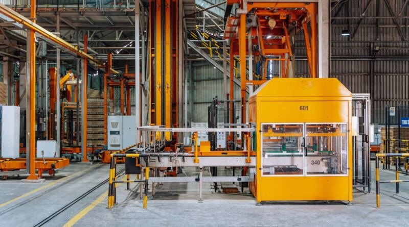 Orange and yellow pallet handling machines in a factory, illustrating latent communication safety between AI agents