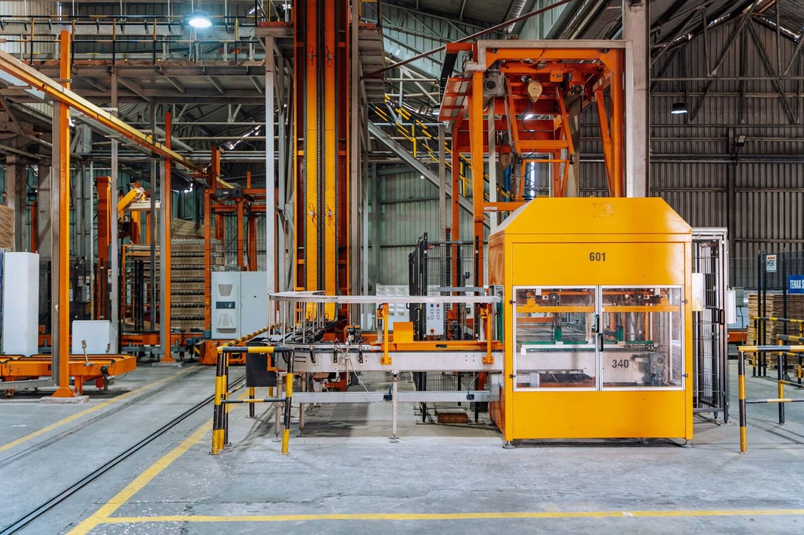 Orange and yellow pallet handling machines in a factory, illustrating latent communication safety between AI agents